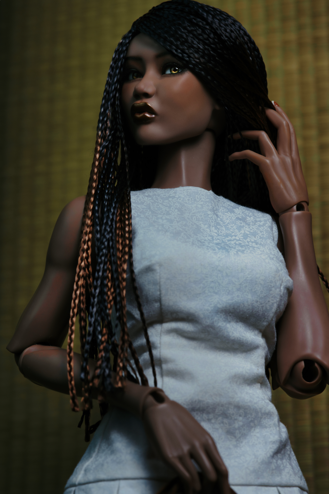 A Black female doll with long straight dark blue hair in a plum blossom dress sitting with one leg crossed over the other on a wooden stool.